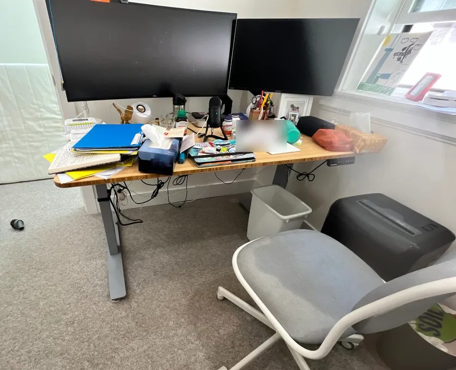David's desk before: papers, folders and supplies piled across the desktop, cables hanging underneath