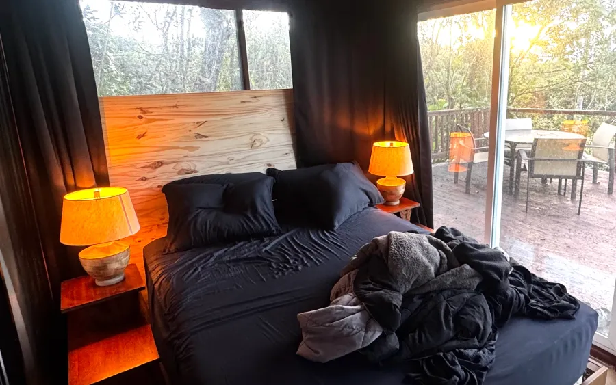 Khris's bedroom after: a solid timber headboard wall and drawn curtains behind the bed, lamps lit