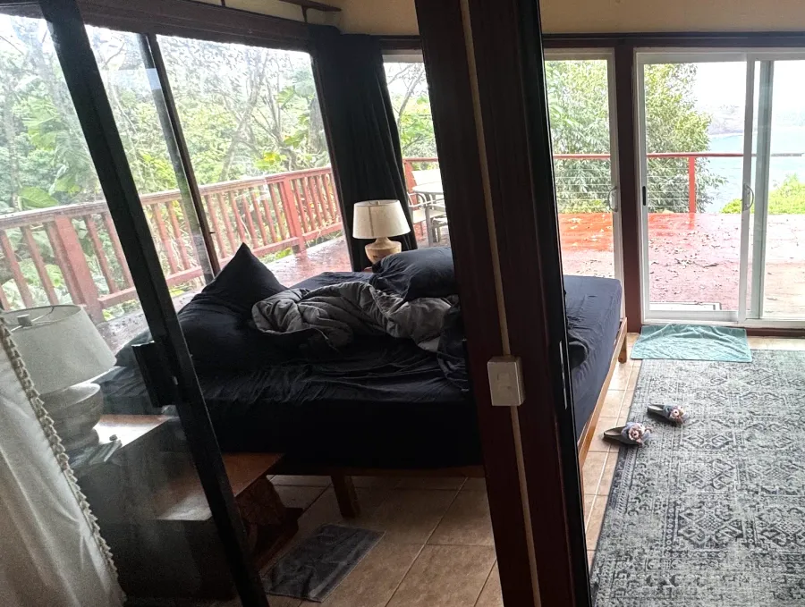 Khris's bedroom before: the bed in a room glazed on every side, open to the deck and the trees